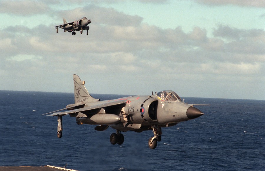 A British Royal Navy FRS.Mk 1 Sea Harrier aircraft hovers over the flight deck of the aircraft carrier USS DWIGHT D. EISENHOWER (CVN 69).  Another Harrier is approaching in the background in 1984 (Photo Source: US Navy)